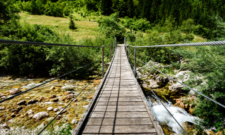 Wooden hanging bridge leading forward over green mountain river. Idyllic mountain river - Lepena valley, Soca â Bovec, Slovenia. Beautiful landscape scene with forest, mountains and river in Slovenia, Europe.の写真素材