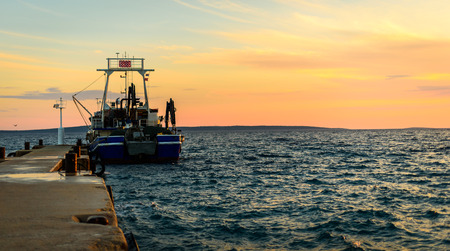 Fishing boat moored or docked at pier in sunset. Commercial fishing ship in the evening at dusk with...