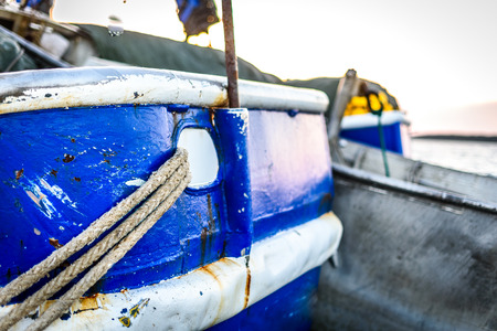 Fishing boat moored or docked at pier in sunset. Commercial fishing ship is tied to pier with thick...