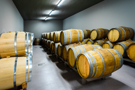 Wooden wine barrels stacked in modern winery cellar in Spain. Modern, contemporary and traditional concrete wine cellar in wine factory - winery with oak barrels kegs with wine. Industrial production.のeditorial素材
