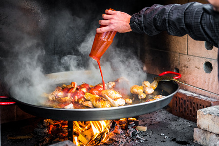 Cooking and making a traditional Spanish Paella over open fire. Traditional way of preparing Valencian paella  with fire wood and flames in a big pan. Made from Chicken and Rabbit meat in fireplace.の写真素材