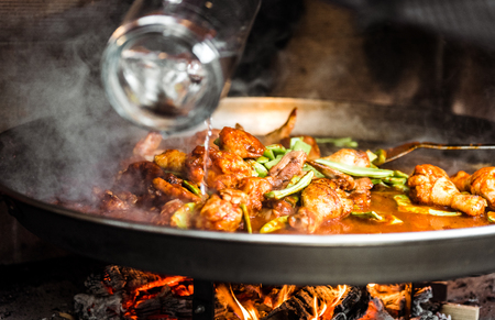 Cooking and making a traditional Spanish Paella over open fire. Traditional way of preparing Valencian paella  with fire wood and flames in a big pan. Made from Chicken and Rabbit meat in fireplace.の写真素材