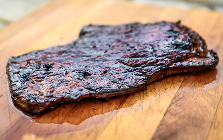Grilled juicy marinated angus beef flank steak on wooden board. Finished juicy medium rare meat is resting before it is cut and sliced.の写真素材