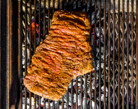 Grilling marinated angus beef flank steak on hot coals barbecue grill. Preparing juicy medium rare meat on hot grill BBQ with grill marks in restaurant fireplace.の写真素材