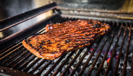 Grilling marinated angus beef flank steak on hot coals barbecue grill. Preparing juicy medium rare meat on hot grill BBQ with grill marks in restaurant fireplace.の写真素材