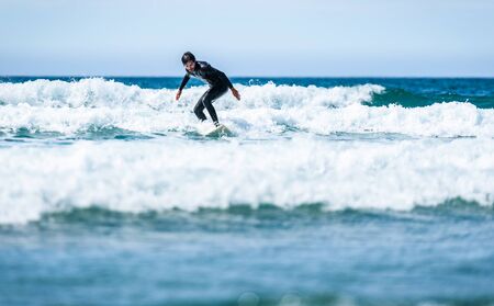 Surfer guy surfing with surfboard on waves in Atlantic ocean. Man in surfing wet suit is active...