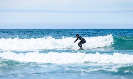 Surfer guy surfing with surfboard on waves in Atlantic ocean. Man in surfing wet suit is active surfing the waves of cold atlantic ocean in Galicia, Spain.の写真素材
