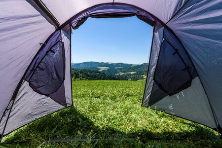 Camping tourist tent set up on meadow in the mountains. Small tent in green mountains of Slovenia. Discovering, hiking on active family vacation in nature with spectacular view of hills and forest.の写真素材