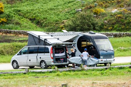 Motorhome RV and campervan are parked on a beach. Surfers on vacation are packing surfboards or...