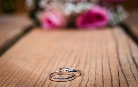 Wedding bouquet with pink roses on wooden table with rings. Wedding rings and beautiful wedding bouquet on natural wooden desk with nature in background. Close up of pink, purple and green flowersの写真素材