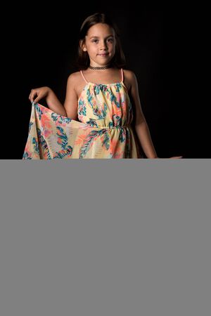 Portrait of happy young little girl holding long colourful dress. Portrait of a cheerful cute little child girl looking at the camera and smiling. Happy children. Isolated on black background.の写真素材