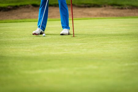Golfer legs at golf tournament practice swing with golf club. Golf players on green lawn putting...