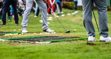 Golfer legs at golf tournament practice swing with driver. Golf players on green lawn putting golf...