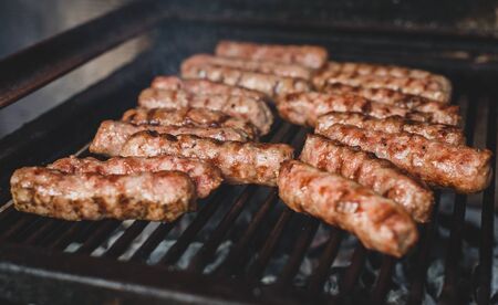 Grilling Meat on barbecue grill with hot coal. Preparing, cooking cevapcici, kebabs, country sausage on charcoal barbecue BBQ in outside fireplace. Traditional Turkish, Bosnian, Serbian, Croatian foodの写真素材
