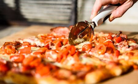 Making of homemade Italian pizza in fireplace brick oven. Making of traditional pizza in stone brick fireplace with fire wood and coals. Cutting finished tasty pizza is perfectly baked with fire.の写真素材