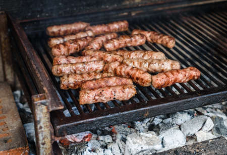 Grilling Meat on barbecue grill with hot coal. Preparing, cooking cevapcici, kebabs, country sausage...