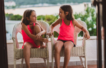 Happy girl kids enjoying summer vacation at sea resort. Family with children on the terrace of a vacation apartment sitting and having fun in the evening. Sea side view in the back. Croatia, Silba.の写真素材