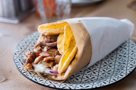 Traditional Greek food gyros pita with fries, vegetables and tzatziki sauce. Close up of kebab...