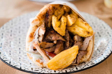 Traditional Greek food gyros pita with fries, vegetables and tzatziki sauce. Close up of kebab...