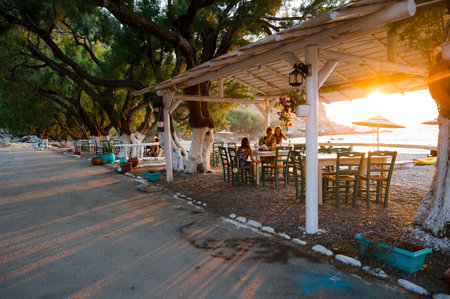 Family enjoying dinner in a restaurant on the beach at sunset. People in a cafeÂ on a beautiful beach tavern with sunset view of the Sfinari beach in Crete, Greece.の写真素材