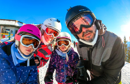Family enjoying winter vacations taking selfie in skiing gear. Family with children on skiing vacation dressed in skiing gear with helmets and ski goggles on sunny day. Winter sports mountain resort.の写真素材
