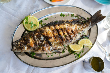Grilled grouper fish on a silver plate in a restaurant in Crete, Greece. Baked fish decorated end...