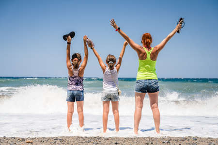 Mother and daughters are standing on the beach on an active family vacation. Family standing and staring at sea, celebrating on a beautiful beach with small stones and sea waves. Crete, Greeceの写真素材