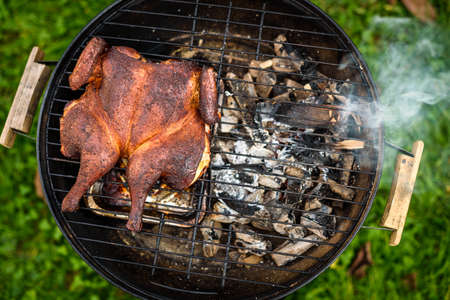 Traditional spatchcocked barbecue chicken al mattone on charcoal grill. Grilling and smoking spatchcock chicken outdoors on firewood BBQ grill in nature on family picnic.の写真素材
