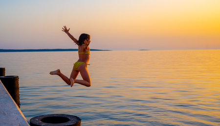 Girl jumping from pier in the water at sunset. Child jumping in the sea in Silba, Croatia.の写真素材