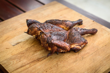 Traditional spatchcocked barbecue chicken al mattone on charcoal grill. Grilling and smoking spatchcock chicken on firewood BBQ grill in nature on family picnic. Ready for cutting on a wooden boardの写真素材