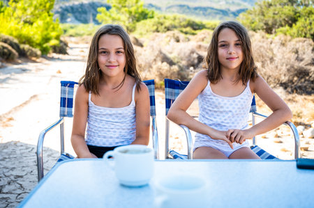 Twin girls eating breakfast in nature camping. Children sitting at camping table on vacation in natureの写真素材