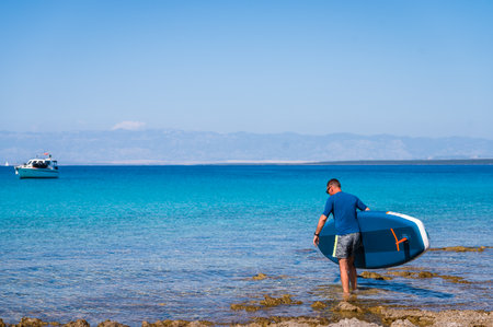 Man riding SUP stand up paddle on vacation. Active male riding SUP boards and paddling in the ocean on a sunny day. Athletic person on SUP board with yachts in background, Silba, Croatia.の写真素材