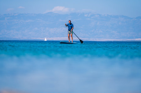 Man riding SUP stand up paddle on vacation. Active male riding SUP boards and paddling in the ocean...