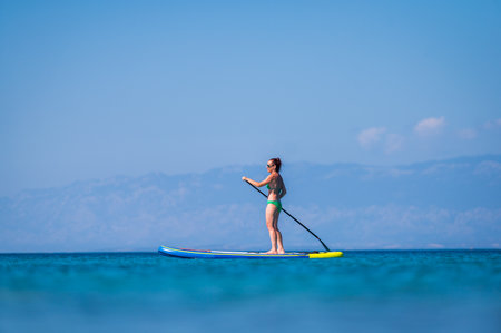 Woman riding SUP stand up paddle on vacation. Active female riding SUP boards and paddling in the...