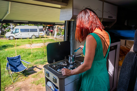 Cooking coffee in campervan, motorhome or RV on camping trip. Woman is making coffee in the morning on a family vacation camping trip onÂ a campsite or camping ground.の写真素材