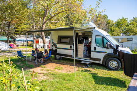 Family camping with a campervan in campsites in Greece or Croatia. Family relaxing with camper van, chairs and table on vacation.の写真素材