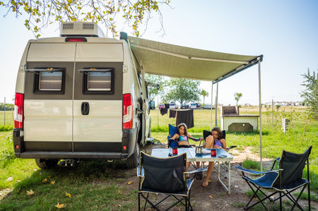 Family camping with a campervan in campsites in Greece or Croatia. Family relaxing with camper van, chairs and table on vacation.の写真素材