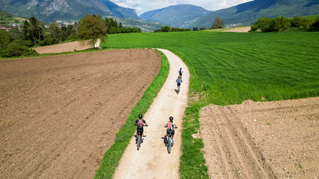 Family on a bicycle trip in nature with mountain bikes. Active family on biking vacation in Italy near Lake Garda is exploring gravel roads through fields and meadows.の写真素材