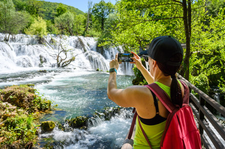 Family visiting famous Martin Brod waterfall in national park Una River in Bosnia and Herzegovina. Tourists taking photos of the amazing waterfall Martin Brod and river Una in Bosnia.の写真素材
