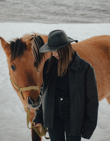 cowgirl with her horse in the snow with hat and leather jacket on a cloudy dayの写真素材