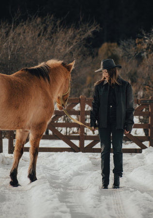 cowgirl with her horse in the snow with hat and leather jacket on a cloudy dayの写真素材