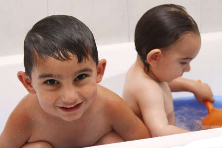 Two little boys are playing in water, smoller play with water (out of focus), older is look to...