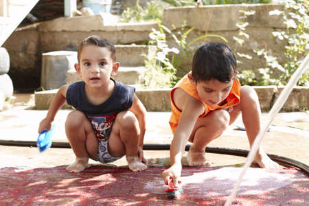 two little boys are washing the red carpet in the yardの写真素材