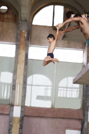 a boy is jumping to swimmingpool from springboard, a man is holding his hands and throw boyの写真素材