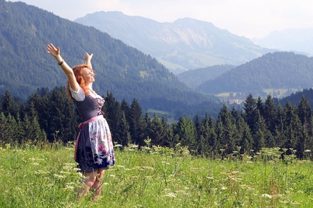a young woman in dirndl looking forward to a mountain meadowの写真素材