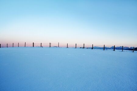 The winter sun has set behind the fence and the mountainsの写真素材