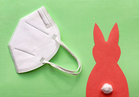 FFP2 protective mask and a red paper Easter bunny on a green background.の写真素材