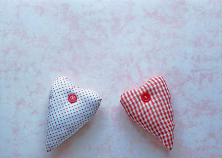 Two red and white fabric hearts on a pink marbled paper backgroundの写真素材