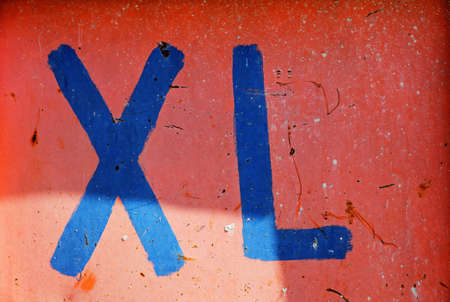 On a red metal wall is written large in blue color XLの写真素材