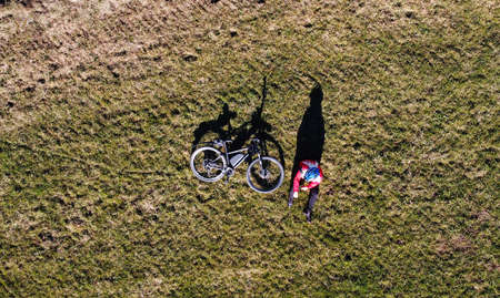 Aerial shot with drone of female cyclist with bike on meadow with light and shadowの写真素材